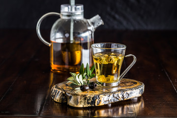 Greek mountain tea with olive leaves on the wood board and a transparent teapot on the wood table. 