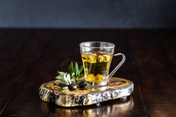 Greek mountain tea in a glass cup and olive leaves on a wooden table. 