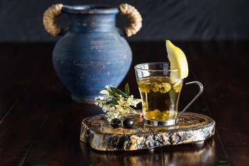Greek mountain tea with lemon in a glass cup and olive leaves with a blue Greek pot background.