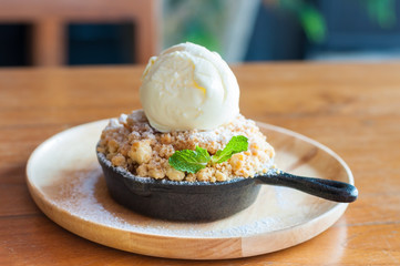 Apple crumble topping vanilla ice cream serve with iron pan and wooden tray on table.