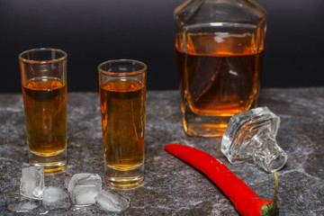 A glass of cognac or whiskey with red pepper on the background of marble.