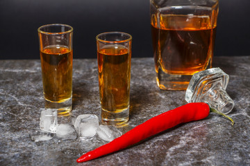 A glass of cognac or whiskey with red pepper on the background of marble.