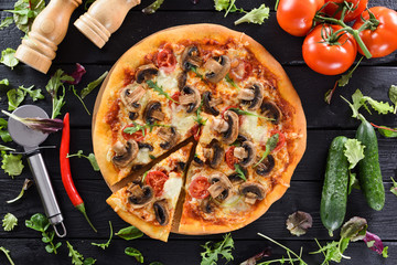 Flatlay of healthy vegetarian fungi pizza, fresh tomatoes, cucumbers, chili and herbs on black...