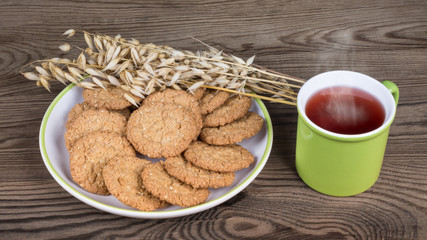 Healthy cookies and mug with hot tea on a wooden background. Pastry from oat flakes with decorative dry oats and the drink with smoke.