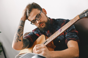 Young guitarist hipster at home with guitar sitting writing melody close-up