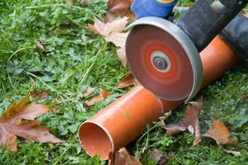 Man with electric circular saw cutting plastic pipe in the garden