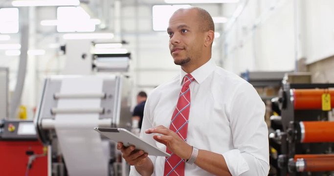 4K Business manager in print factory working on computer tablet. Crane shot panning upwards offering interesting change of background.
