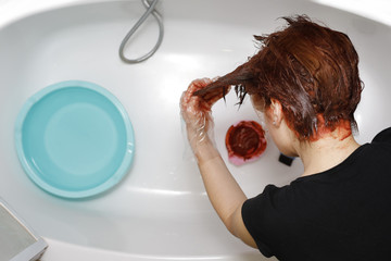 Woman in process of hair coloring at home. Applying red color to the hair in the bathtub..