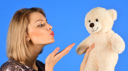 Woman holds teddy bear on blue background.