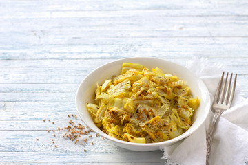 Pickled chinese cabbage with garlic and spices, mustard, turmeric, hot pepper in a white bowl on a blue background, selective focus, free space. Healthy oriental food