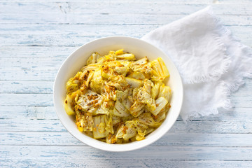 Pickled chinese cabbage with garlic and spices, mustard, turmeric, hot pepper in a white bowl on a blue background, selective focus. Healthy oriental food