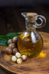 Natural macadamia oil in a glass bottle with macadamia nuts on wooden board.