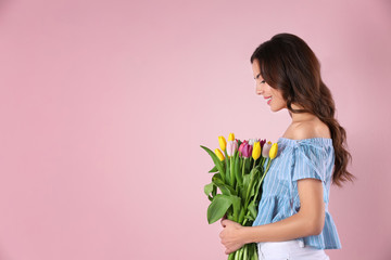 Beautiful woman holding bouquet of tulips on color background