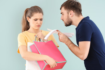 Woman holding shopping bags and man with bills arguing about money on color background. Problems in...