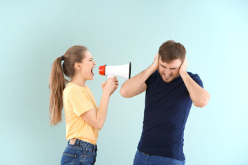 Young woman shouting into megaphone at man on color background. Problems in relationship