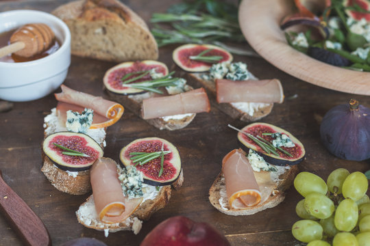 Easy diet salad with arugula, figs and blue cheese on a brown wooden surface. Sandwiches with ricotta, fresh figs, prosciutto, rosemary and blue cheese. Delicious fruity breakfast, top view. Toned.