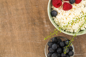 Cottage cheese in bowl with raspberries and blueberries on wooden background. Healthy breakfast .Flat lay. Place under the text
