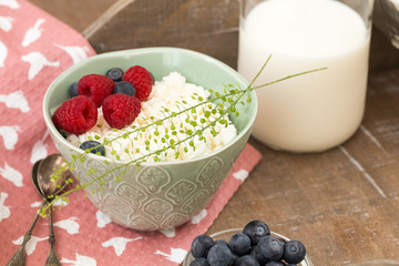Cottage cheese in blue bowl with raspberries and blueberries and milk on wooden background. Healthy breakfast