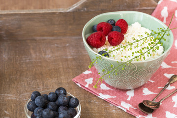 Cottage cheese in bowl with raspberries and blueberries on wooden background. Healthy breakfast .Place under the text