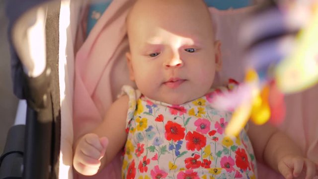Slow motion shot of a baby girl in colorful onesie lying in pram outdoor on sunny summer day