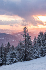 Obraz premium Malowniczy zachód słońca zimą w górach z widokiem na las