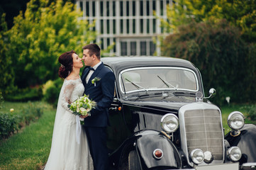 stylish bride and groom sensually posing near retro car with boh