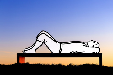 Lying man on a bench at sunset