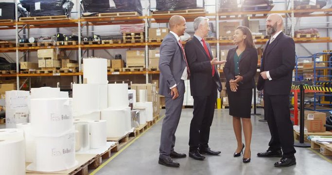 4K Cheerful business team in suits chatting in large warehouse