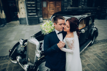 stylish bride and groom sensually posing near retro car with boh