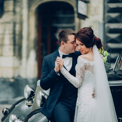 stylish bride and groom sensually posing near retro car with boh