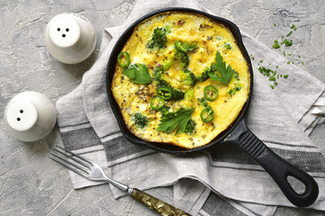 Rustic omelette with broccoli and cheese in a black iron pan.Top view.