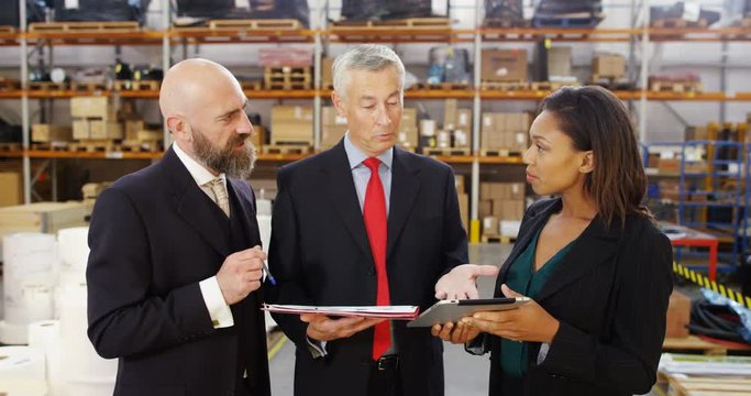 4k, Multi ethnic business people with digital tablet and paperwork discuss inventory in a warehouse.