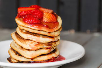 Delicious Strawberry Pancakes on a dark moody background, stunning breakfast with vibrant colors, white plate