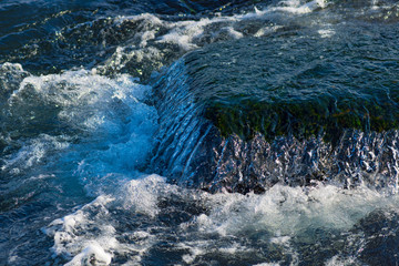Still close-up image of running water at dark green rocks covered with moss