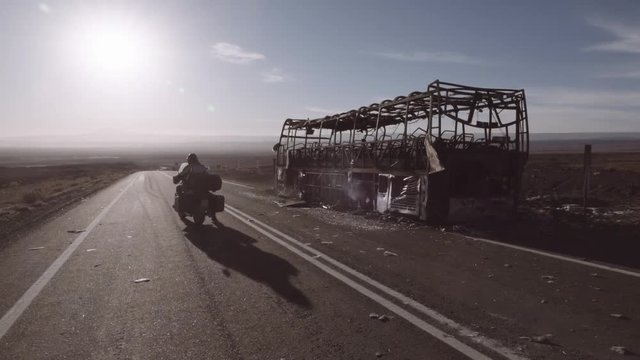 Motorcyclist stops next to a burnt bus to assist. 