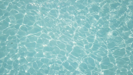 Fototapeta na wymiar Water in swimming pool rippled water detail background. Water in swimming pool with sun reflection. Blue swimming pool rippled water detail