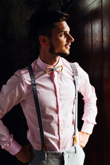 A guy in gray trousers with suspenders holds his arms in his waist and looks seriously