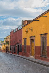 Colorful homes of red and yellow, lining a cobblestone street and stone sidewalk, in San Miguel de Allende