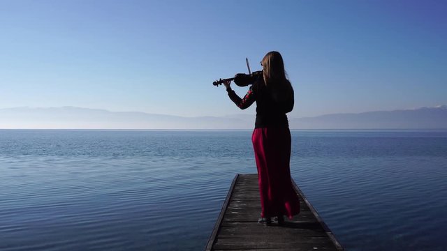 Young female violinist playing violin while standing on wooden pier by Ohrid Lake, Macedonia