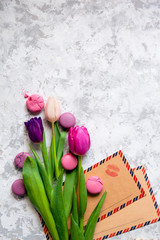 Pink and purple tulips and macarons and vintage kraft envelopes with kiss print on light textured background. Romantic congratulations concept with copy space.