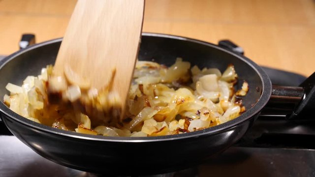 Chopped onions fried  in hot frying pan, hand mixing with wooden spoon spatula. Vegetable preparing, meals with vegetables. Slow motion