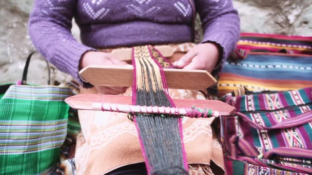 Indigenous woman weaves yarn a foot loom at downtown Cusco, Peru. Slow motion