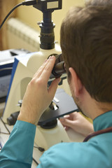 Young handsome doctor checking the blood sample on his microscope in his medical office