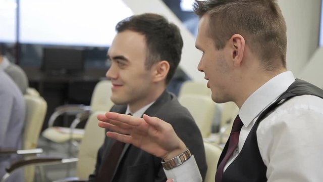 The tro businessmen discuss the presentation sitting on the confernce in bright office. The professional in the vast and tie explains his point and the manager in suit nods his head to agree. The