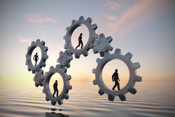Gears of teamwork at sea at sunset. Executives walking inside gears at sea at sunset demonstrate the power of cooperation and synergy