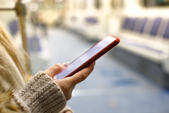oncept-woman holding smart phone closeup in empty metro train, blurred background/ Young girl using cellphone,  reading interesting e book or text messages, checking news feed, side view, copy space 