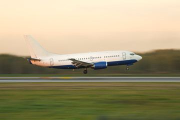 Fototapeta na wymiar narrow-bodied passenger airplane landing at international airport during sunset, in motion, side view, copy space for text/ airplane climbs after take off/ Landing aircraft low over the runway