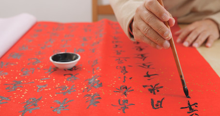 Fototapeta na wymiar Asian man writing chinese calligraphy on red paper
