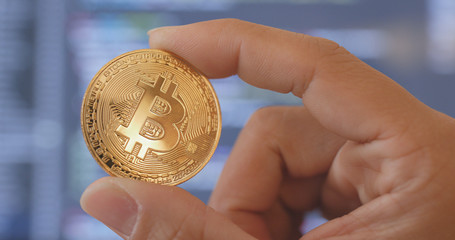 Hand holding bitcoin over the computer screen