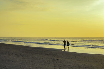 Woman and man walking o a beach at sunrise